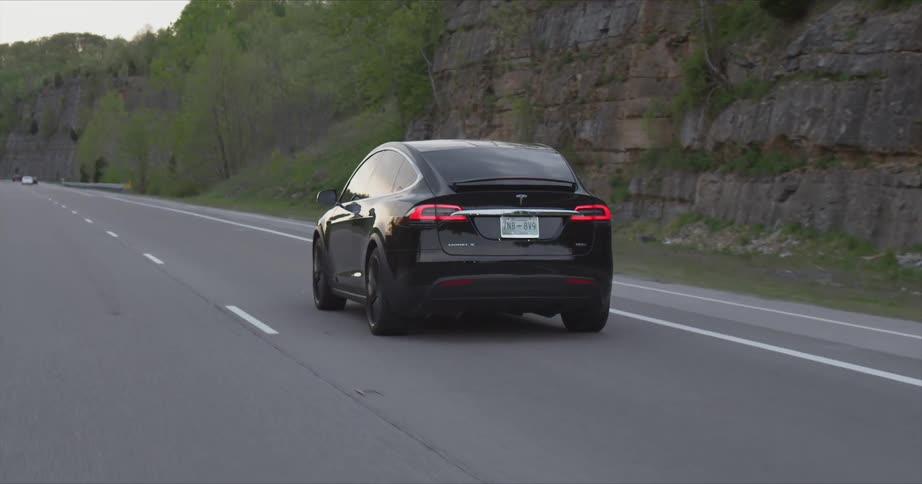 A black car drives past the mountains on the road