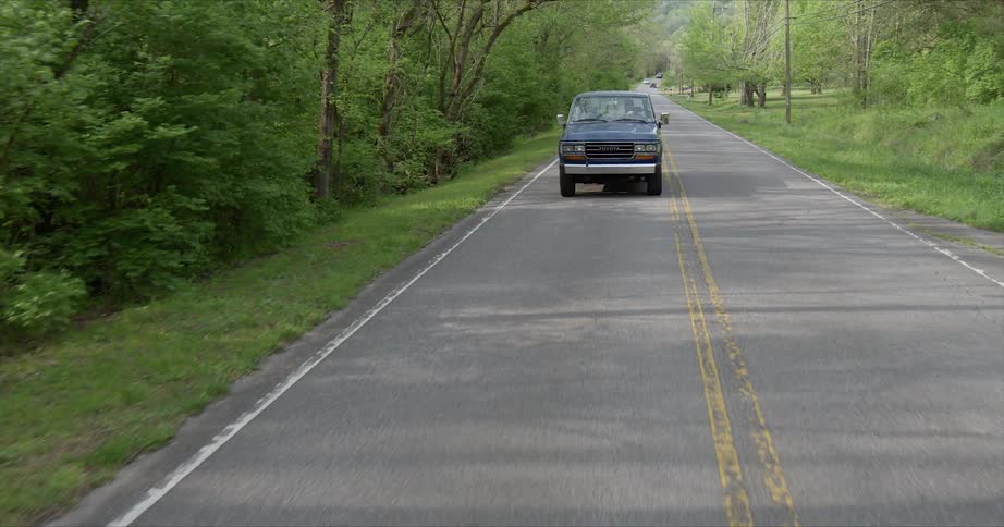 A person is driving a pickup truck on a rural road in daylight