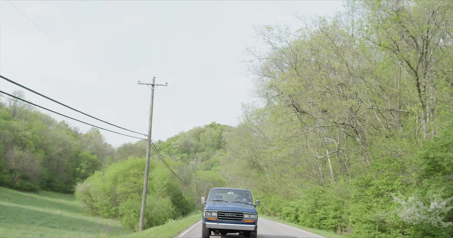 A pickup truck is driving on a rural road in daylight