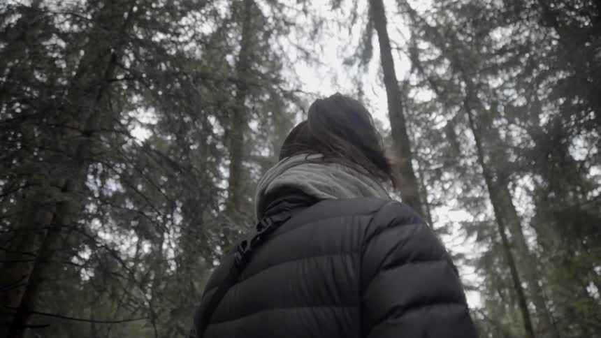 A woman looks up at the trees and walks into the forest