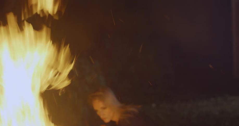 Fire blazes at night and a woman dances next to it