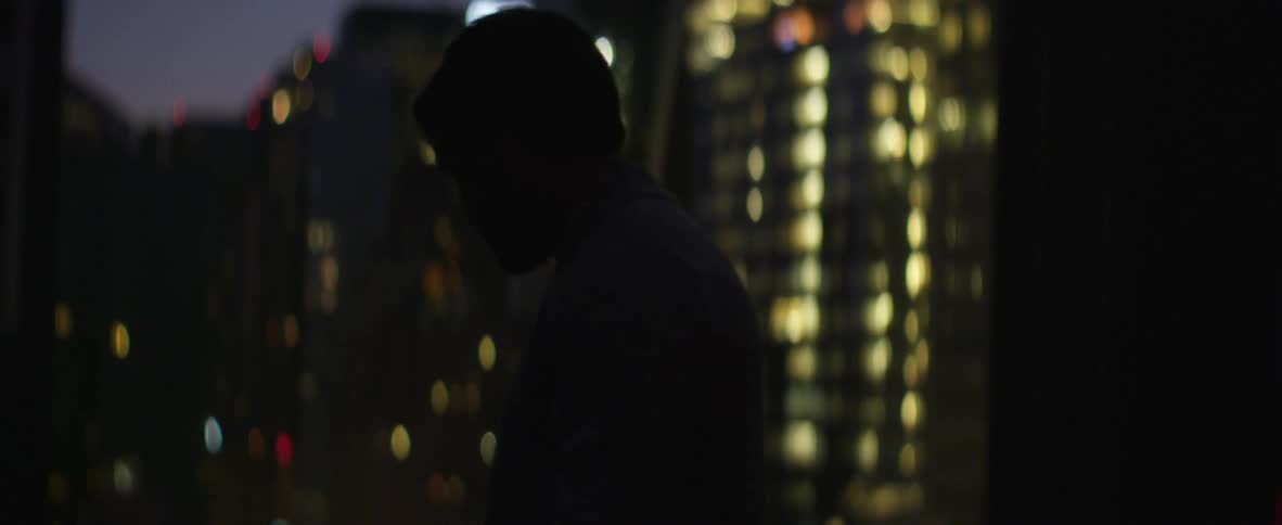 Man smoking a cigarette in front of some buildings at night