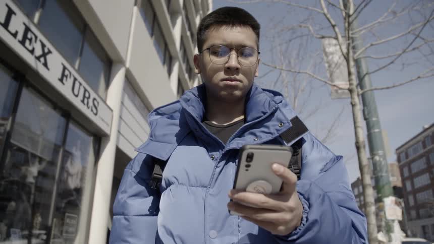 A young man uses his phone while walking outside