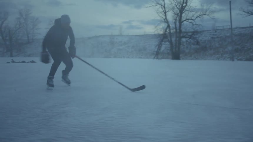 A man holding a hockey stick skates on a frozen pond