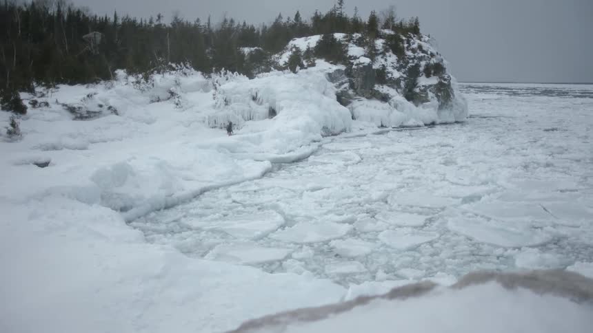 A person walks near the shore covered with ice