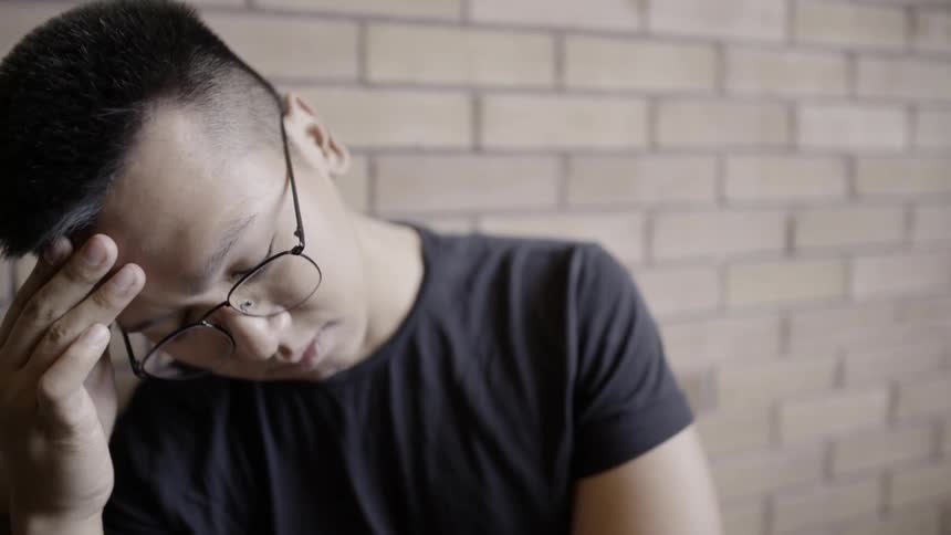 A man is deep in thought as he leans against a wall in daylight