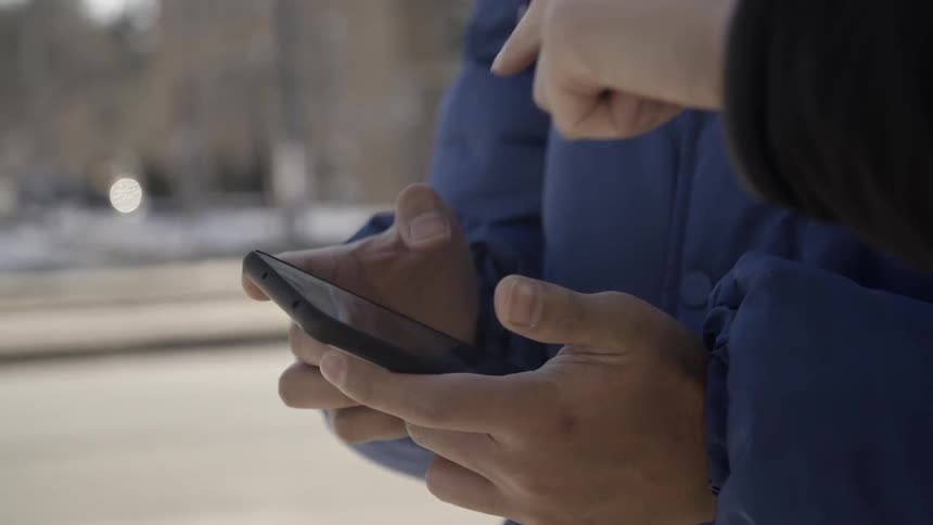 Two people use a phone together outside