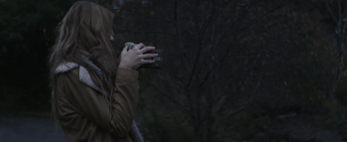 A young woman stands next to trees and takes a photograph