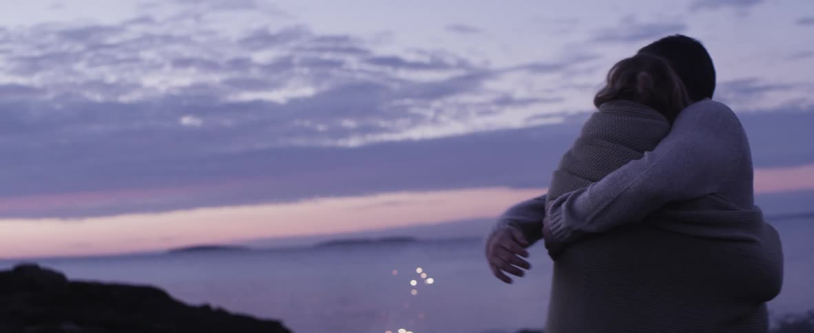 Man and woman embrace as fireworks go off at sunset