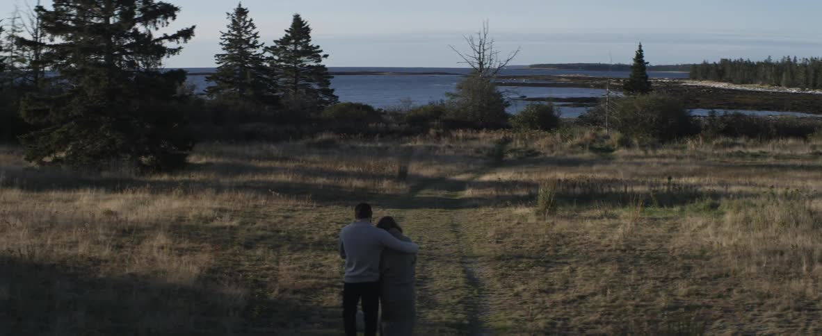Man and woman walk towards the water over a grass field