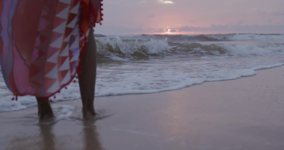 Person stands on the beach as water washes over their feet at sunset