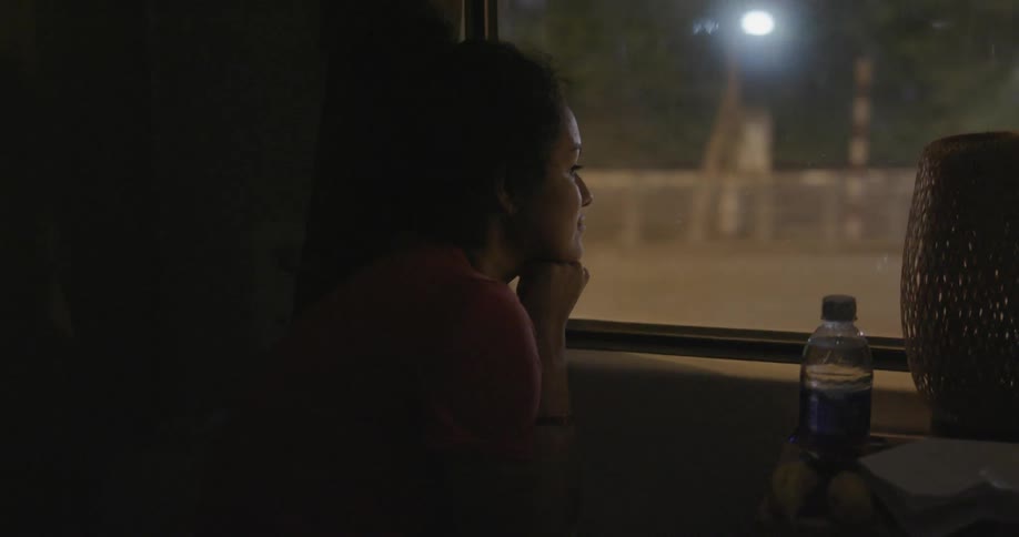 Woman sits on a bus looking out the window at a city at night