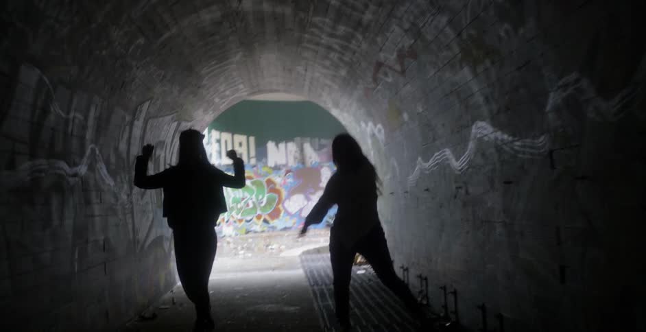 Two woman are dancing in a city tunnel