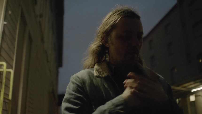 A man is rubbing his hands as he stands outside in a city on a cold night