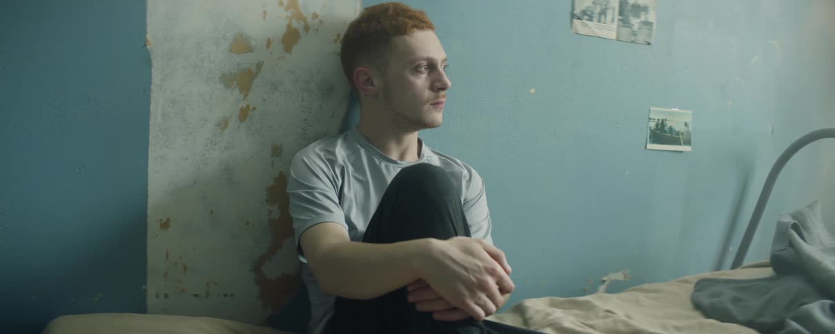 Young man sits on bed thinking