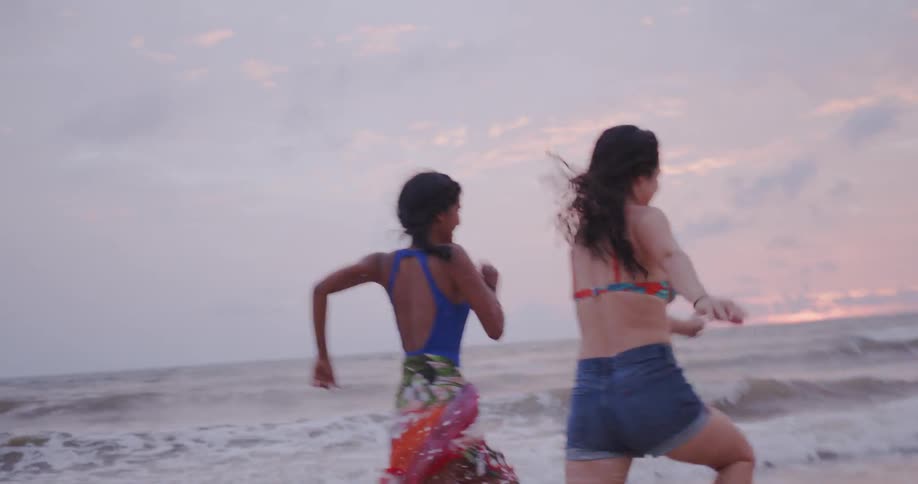 Two women run on a beach at sunset