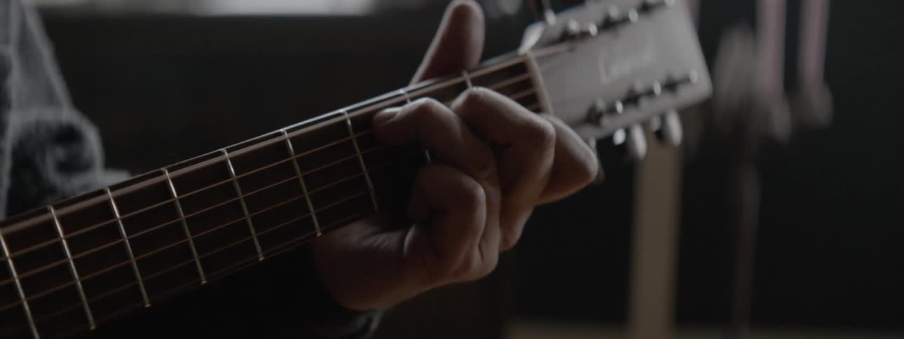 A man is playing a guitar inside a room in daylight