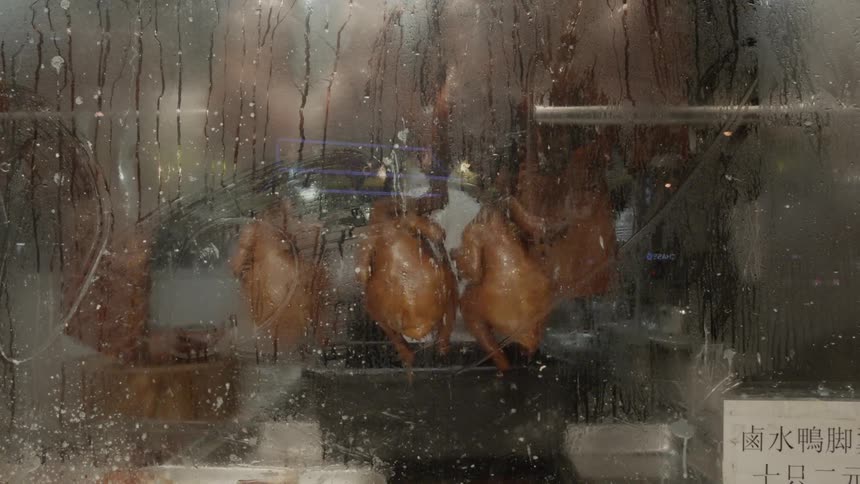 Roasted chickens hang behind glass