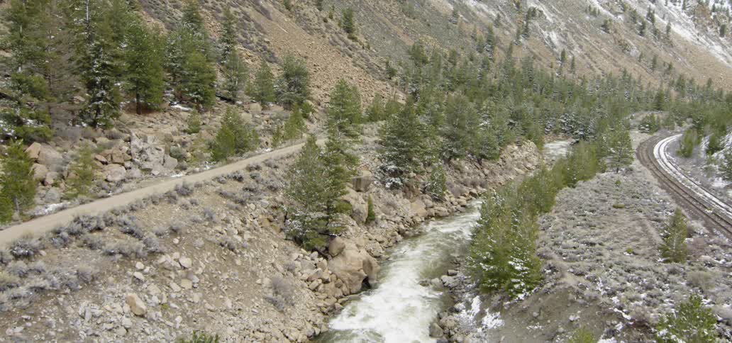River flowing in between dirt road and railroad tracks