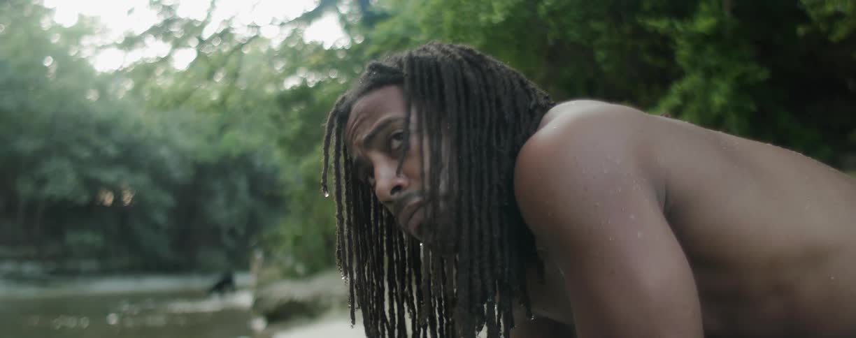 Shirtless man sits by a river