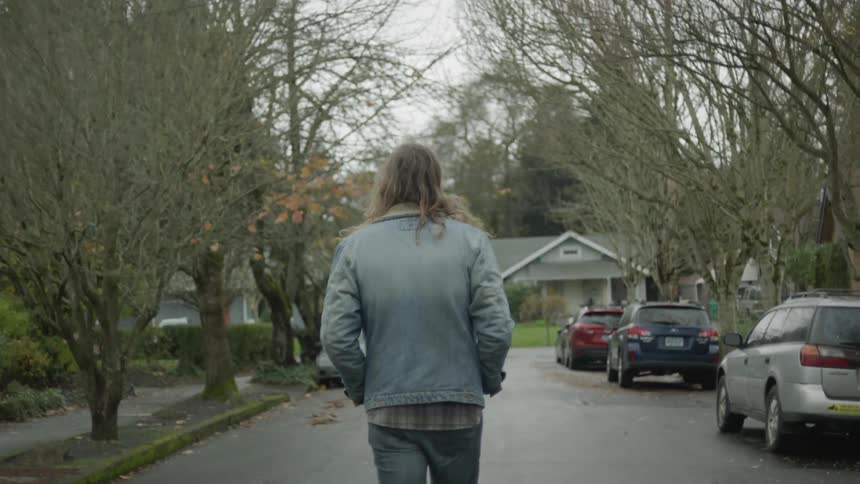 The man is walking down the neighborhood street