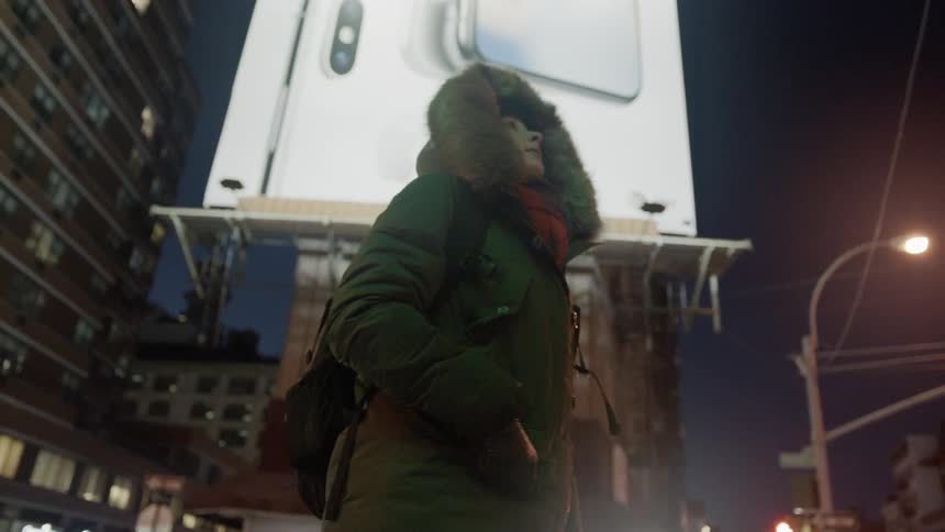 The woman stands in front of the billboard looking around