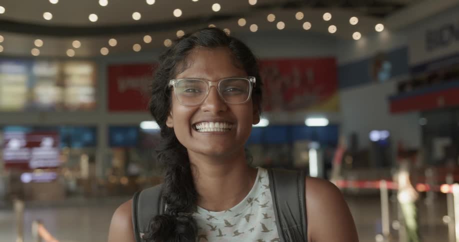 A woman is smiling broadly as she stands inside in daylight