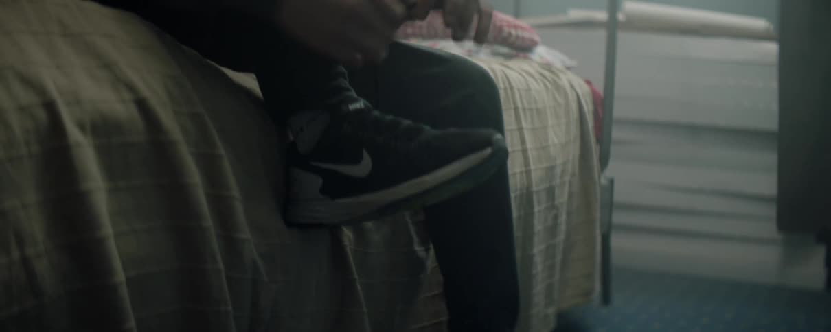 Man puts on sneakers while sitting on a bed