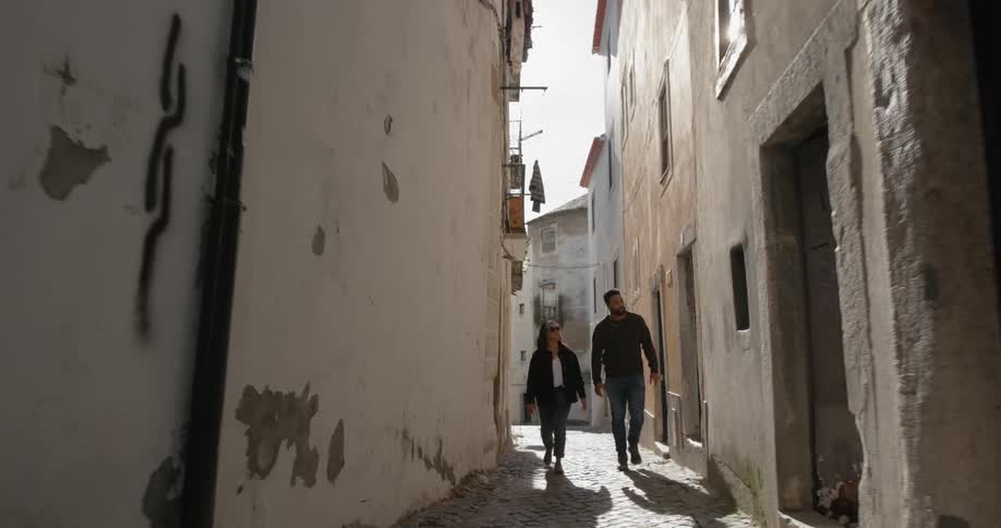 A man and a woman walk down a narrow alleyway between buildings at day time