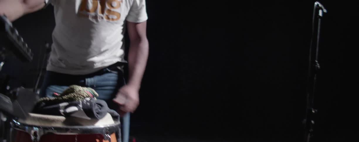 Man picks up a piece of equipment and fastens it to his drum set