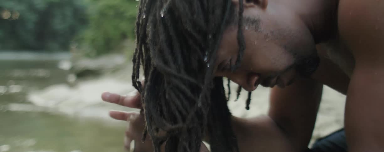 Man is wringing water from his dreadlocks by river