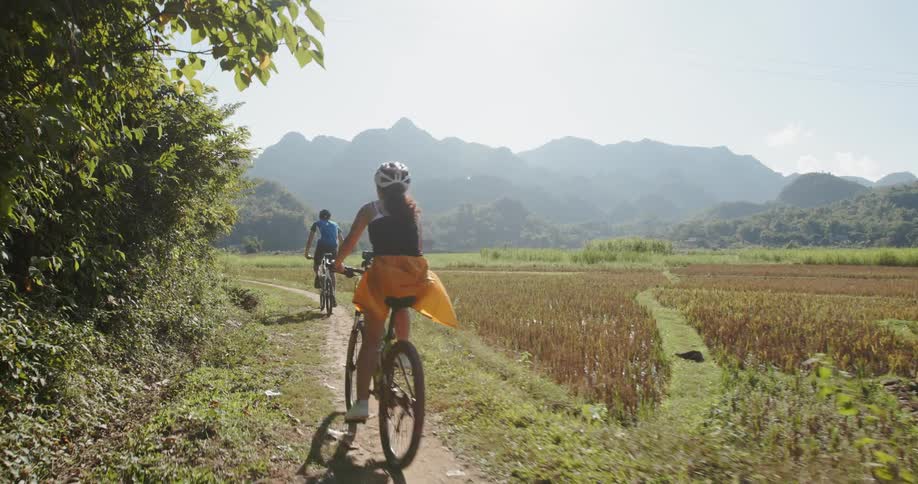 Group of people ride bicycles on a trail near a field