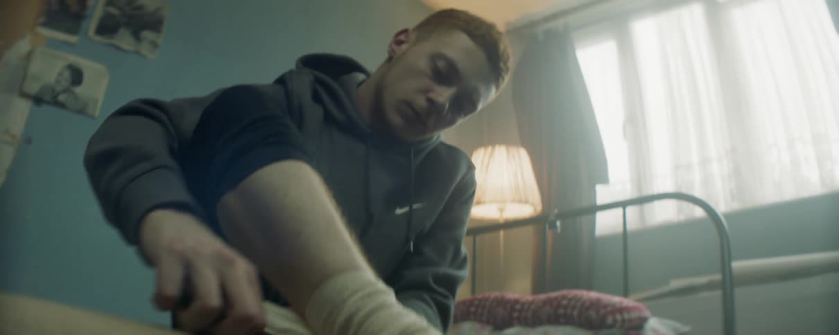 Man wraps his ankle while sitting on a bed