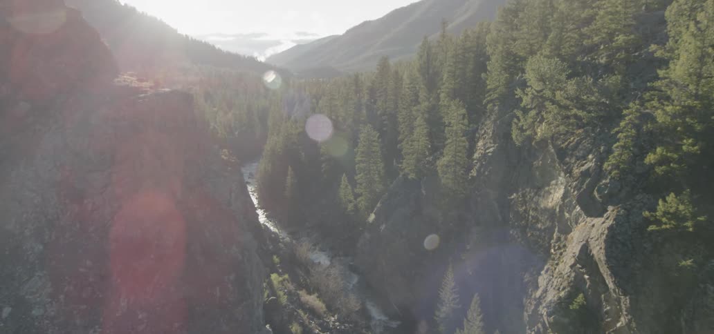 Sunlight is beaming down on a river rushing through a ravine