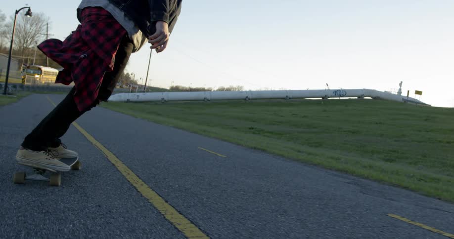 Man skateboards on a road at sunset