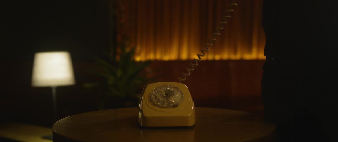 A person answers a rotary phone on a table then hangs up
