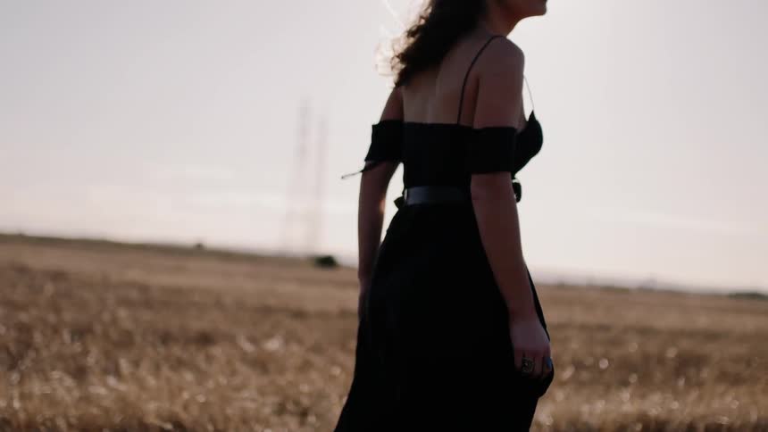 Woman in a black dress walks in a field under the bright sun