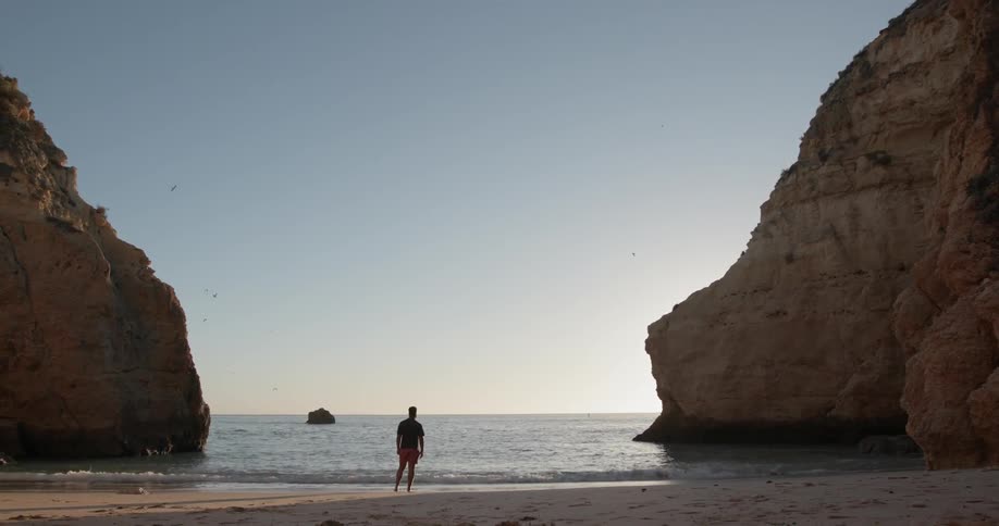 Man is standing on ocean beach between large rock formations