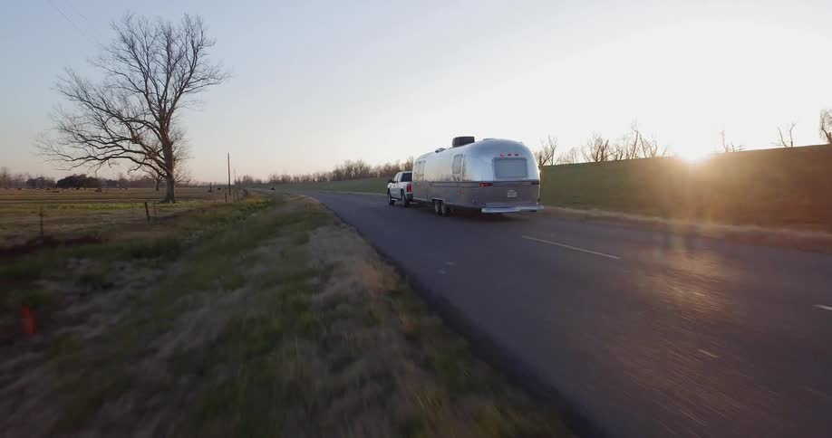 Truck pulls a trailer on a rural road at sunset