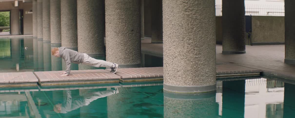 The man is doing push ups near the pool