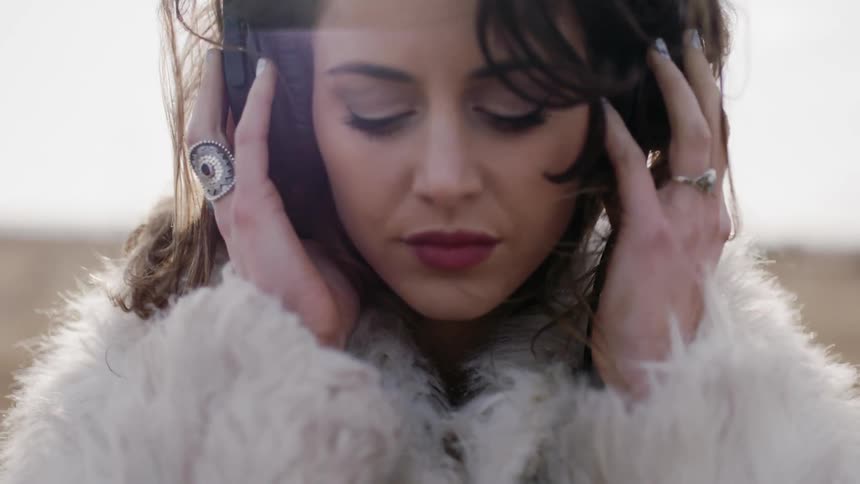 Woman listens to headphones outside on a windy day