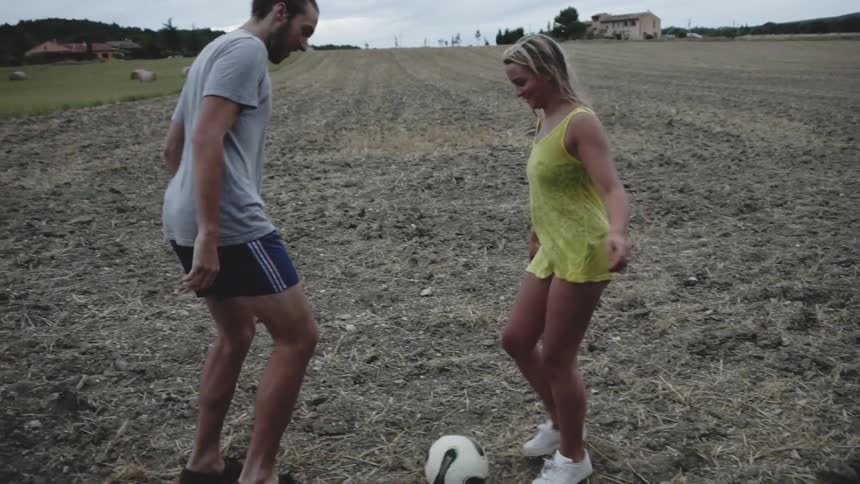 Man and woman are kicking soccer ball in dry field
