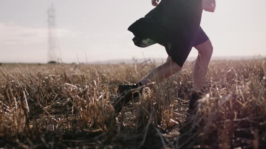 Woman in a black dress runs through a field under a sunny sky