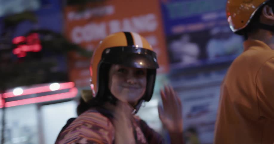 A woman smiles and poses as she rides on the back of a bike in the city at night