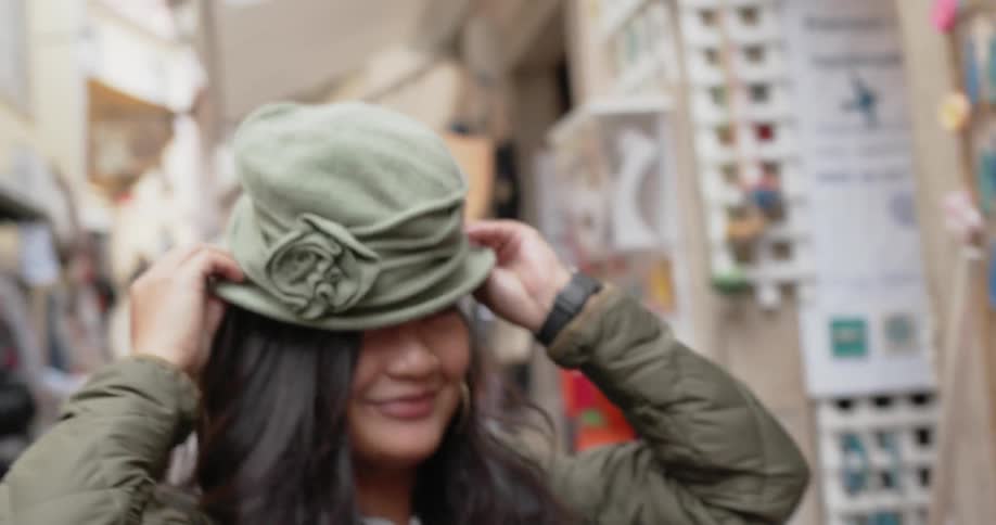 Woman smiles while trying on a hat at an outdoor market