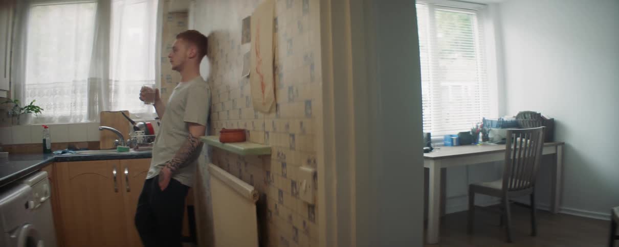 A man leans against the wall drinking from a glass