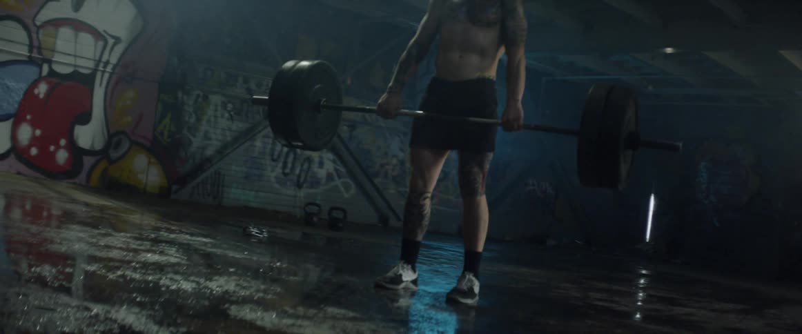 Man lifts a large barbell in a dim room