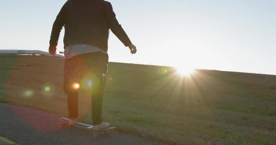 A man rides a skateboard on a park path at sunset