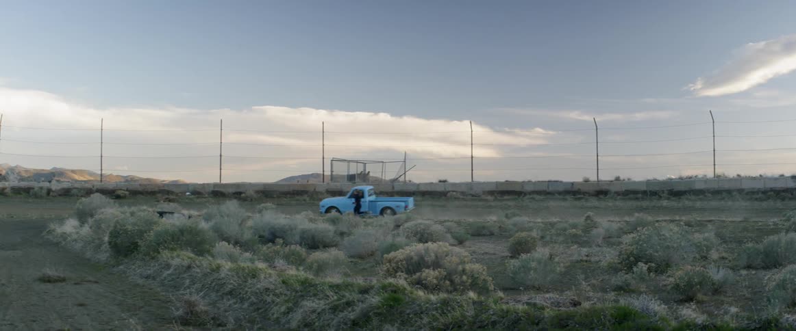 A pickup truck is pacing a woman as she is jogging in a desert in daylight
