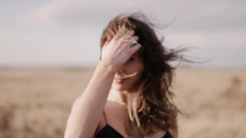 Woman in a black dress pushes the hair away from her face as she stands in a field